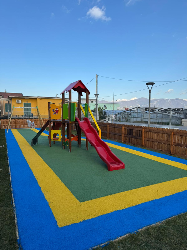 Parco giochi colorato con scivolo su una superficie di gomma blu e gialla sotto un cielo limpido.