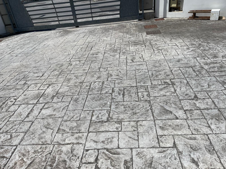 Cortile pavimentato con motivi in pietra, adiacente a un cancello metallico e al muro di cinta dell'edificio.