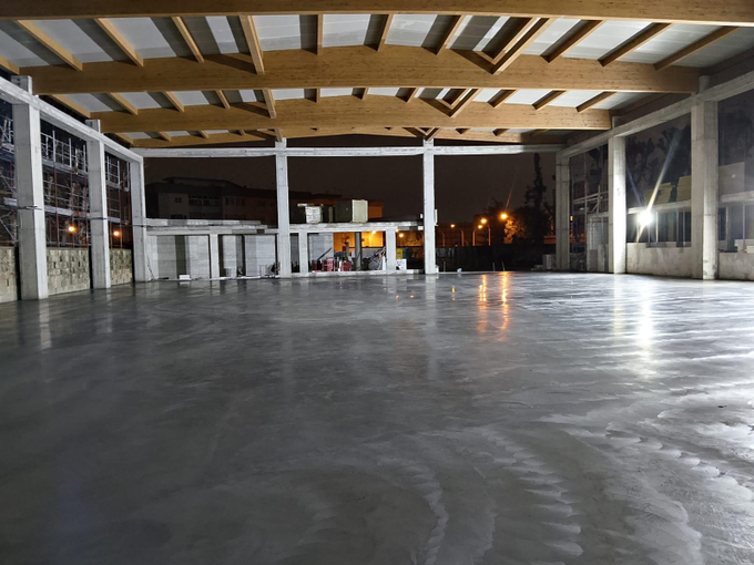 Patio coperto vuoto con pavimento in cemento bagnato, travi in ​​legno a vista e pareti di vetro scuro di notte