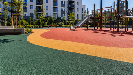 Parco giochi colorato con scivoli e strutture per arrampicarsi accanto a moderni palazzi residenziali.