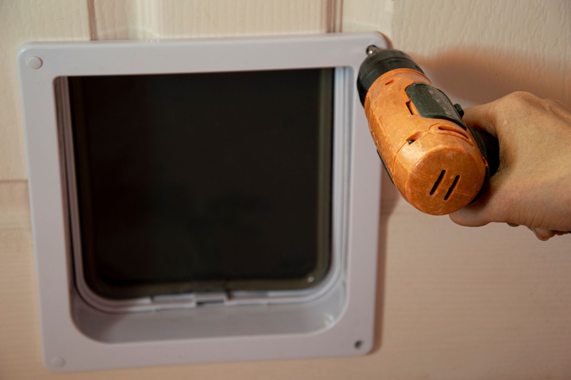 A close-up of a hand using a power drill to install a dog door.