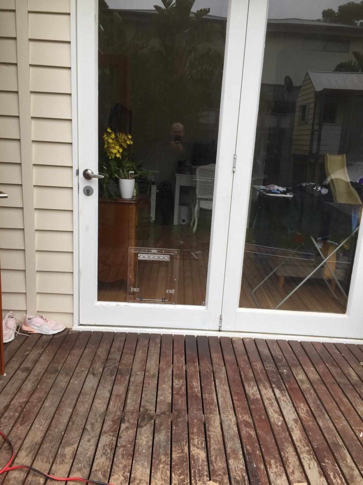 Wooden deck outside a glass patio door with a table, chairs, and indoor plants visible inside