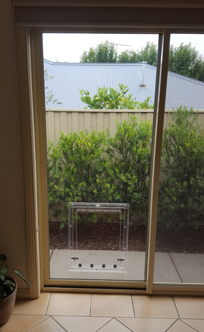 Sliding glass door to a patio with bushes, a small table, and a fence outside.