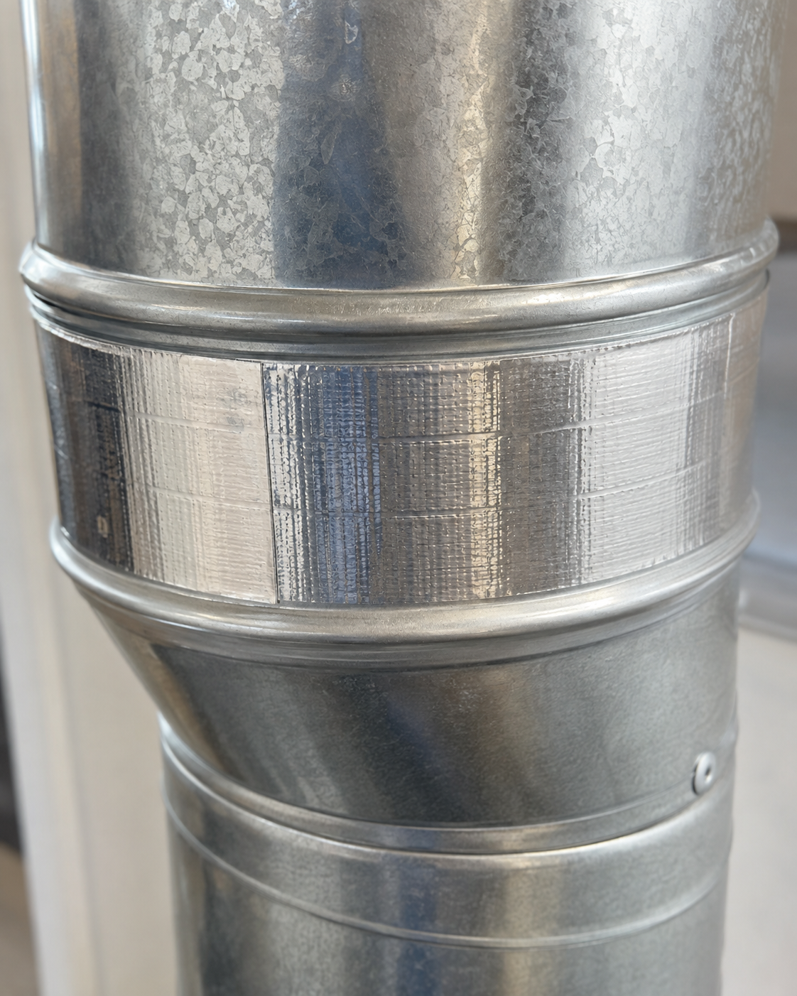 Close-up of a silver metal duct with a banded seam and rivets