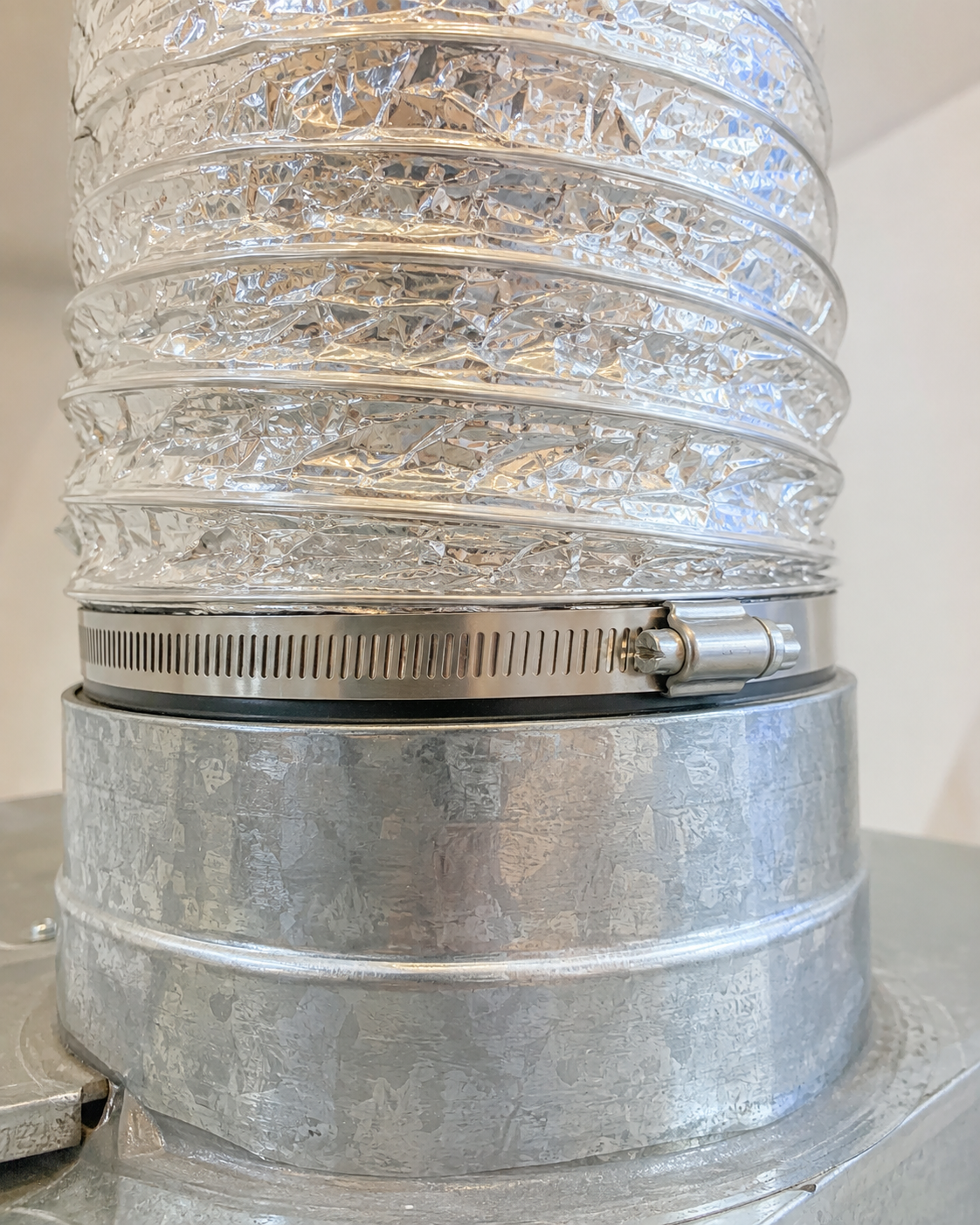 Silver flexible vent hose attached to a round galvanized metal duct fitting with a clamp