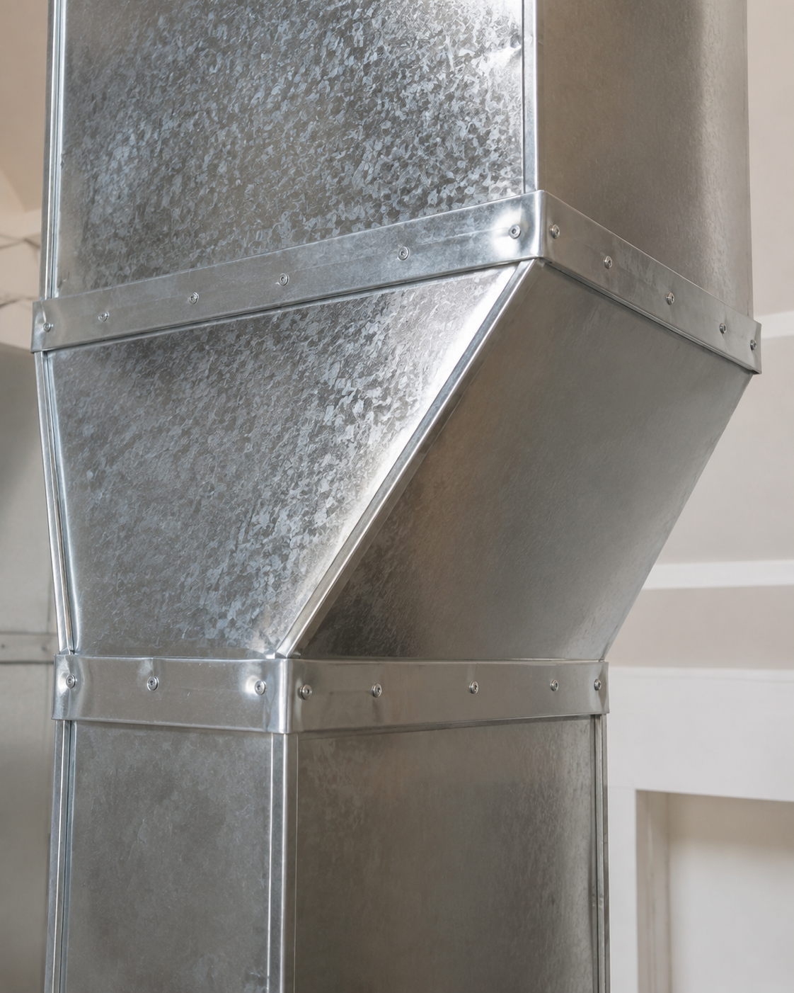 Galvanized metal HVAC ductwork with angled joints against an indoor wall