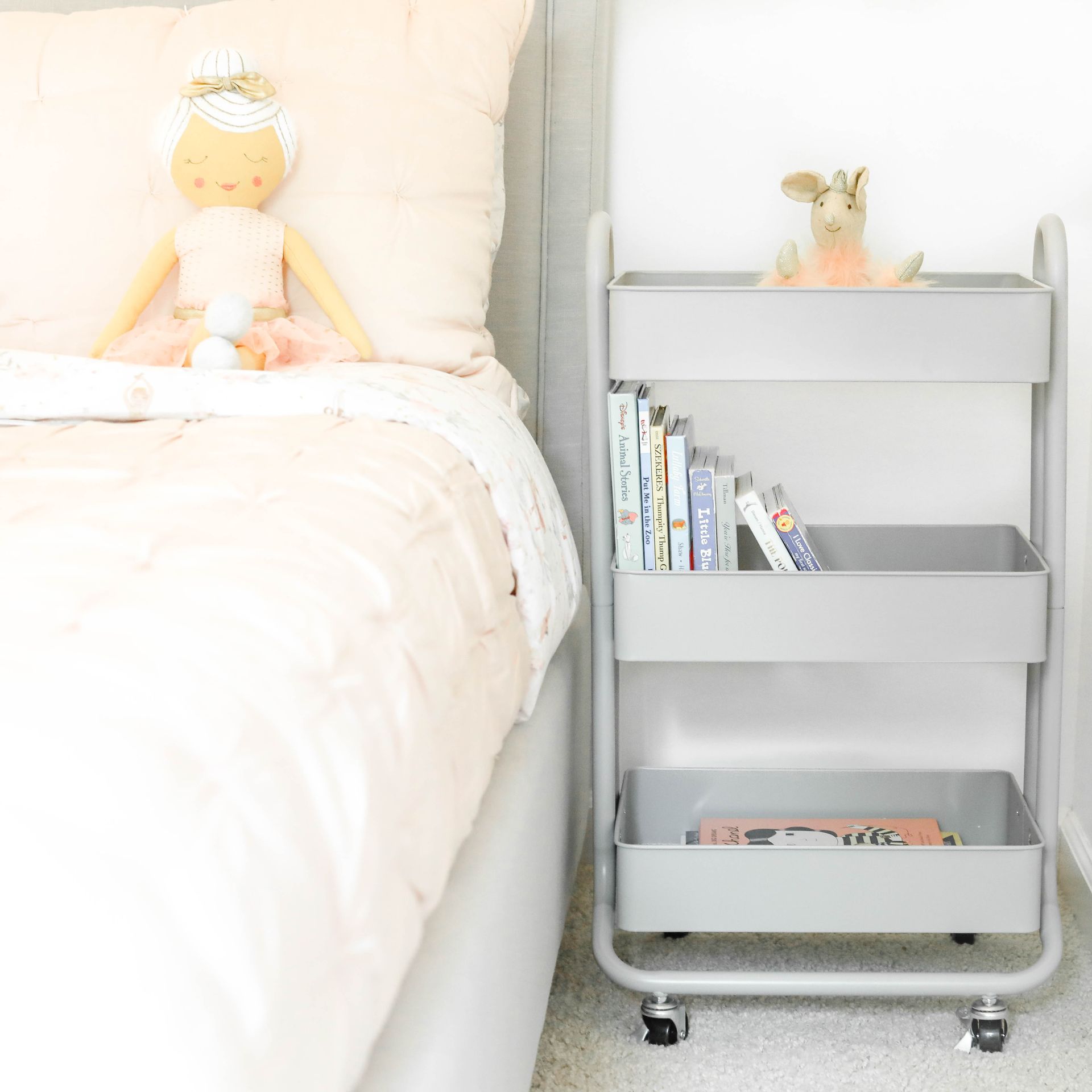 A doll is sitting on a bed next to a cart with books on it.