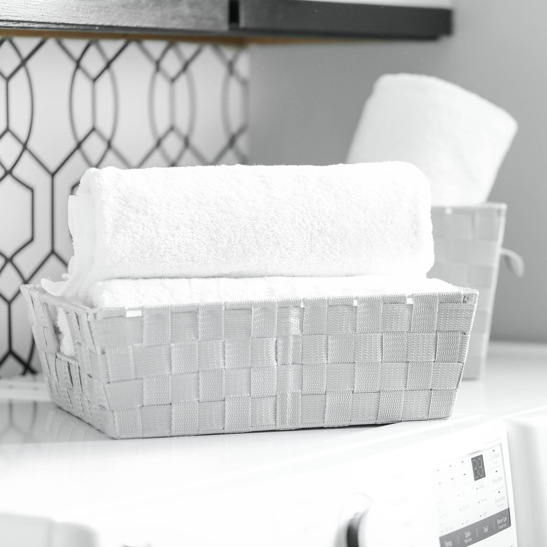 A white basket filled with white towels is sitting on top of a washing machine.