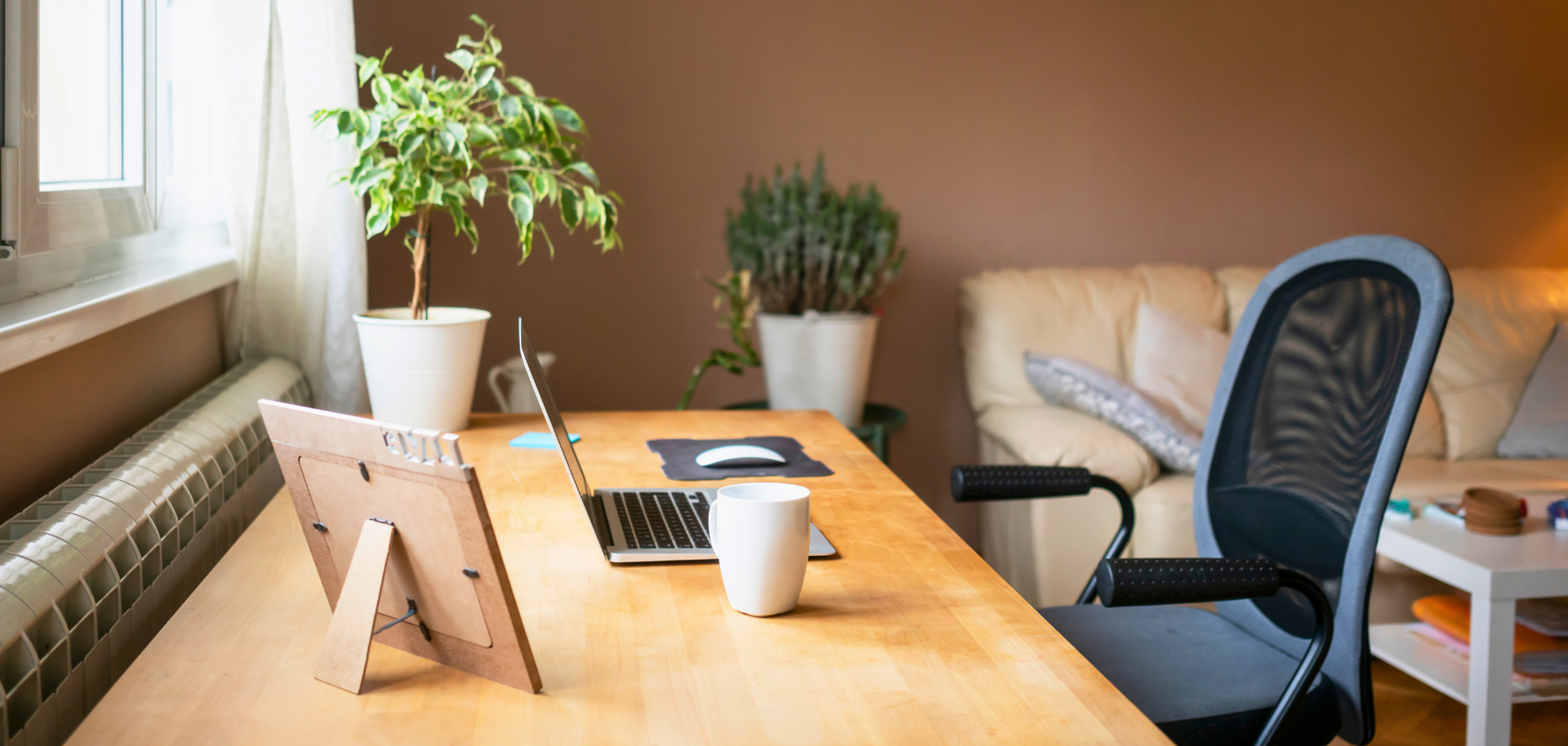 A wooden desk with a laptop and a picture frame on it in a living room.