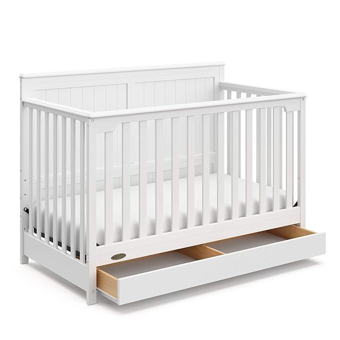 A white crib with a drawer underneath it on a white background.