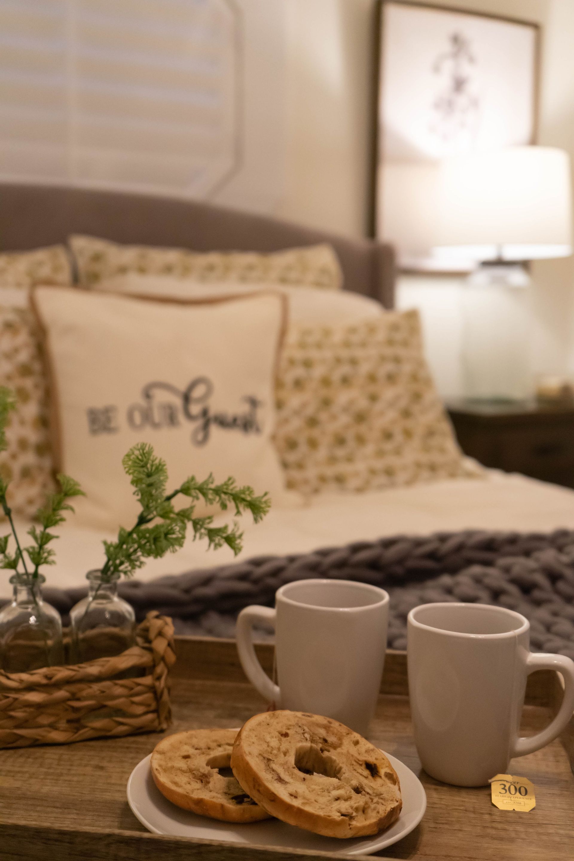 A tray of bagels and two cups of coffee on a bed.