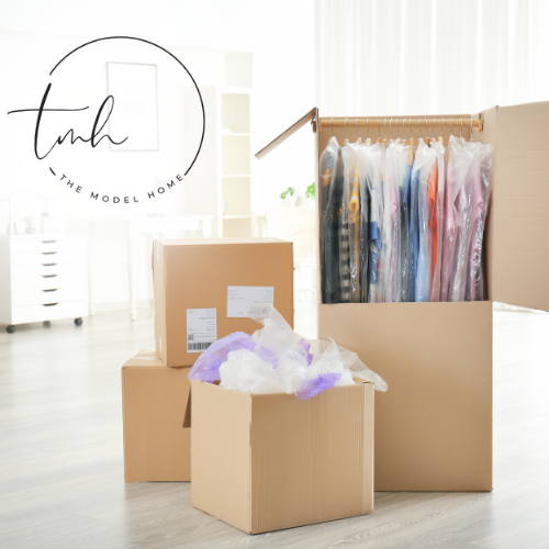 Three cardboard boxes are stacked on top of each other with a logo for the model home