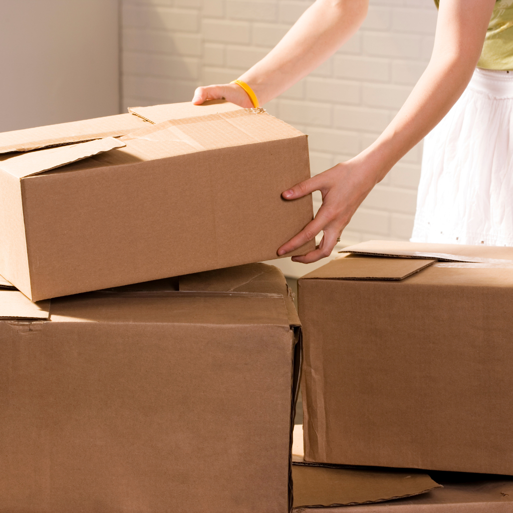 A woman is putting a cardboard box on top of a pile of cardboard boxes