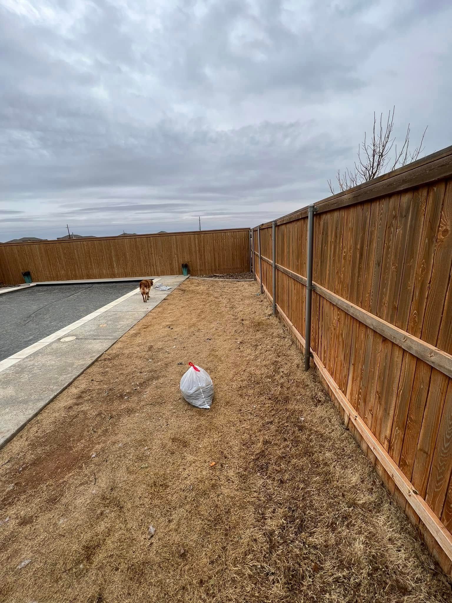 Backyard with wood fence, gravel path, and cloudy sky; a plastic bag lies on the ground.
