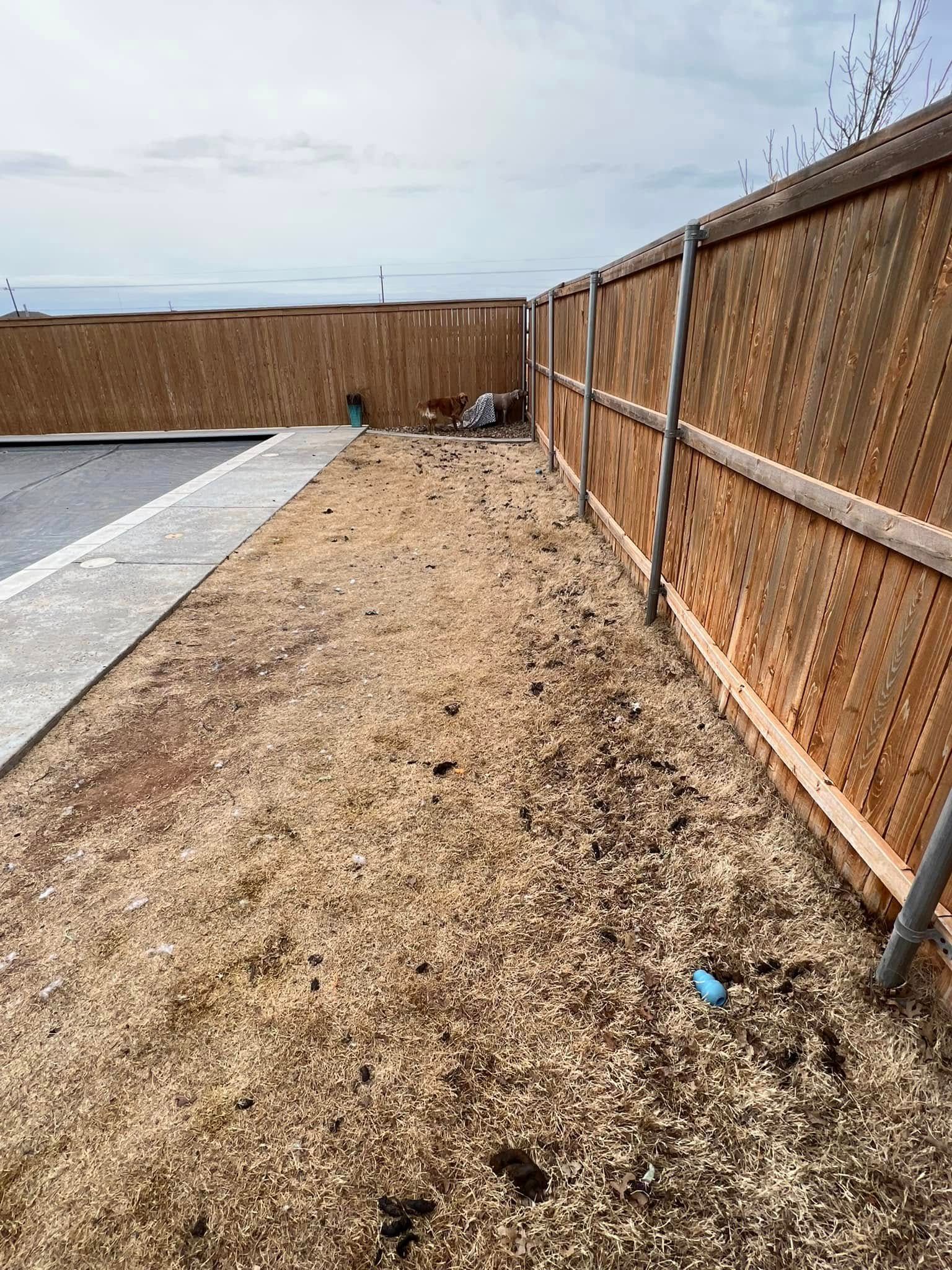 Gravel strip beside a parking lot, bordered by a wooden fence under a cloudy sky.