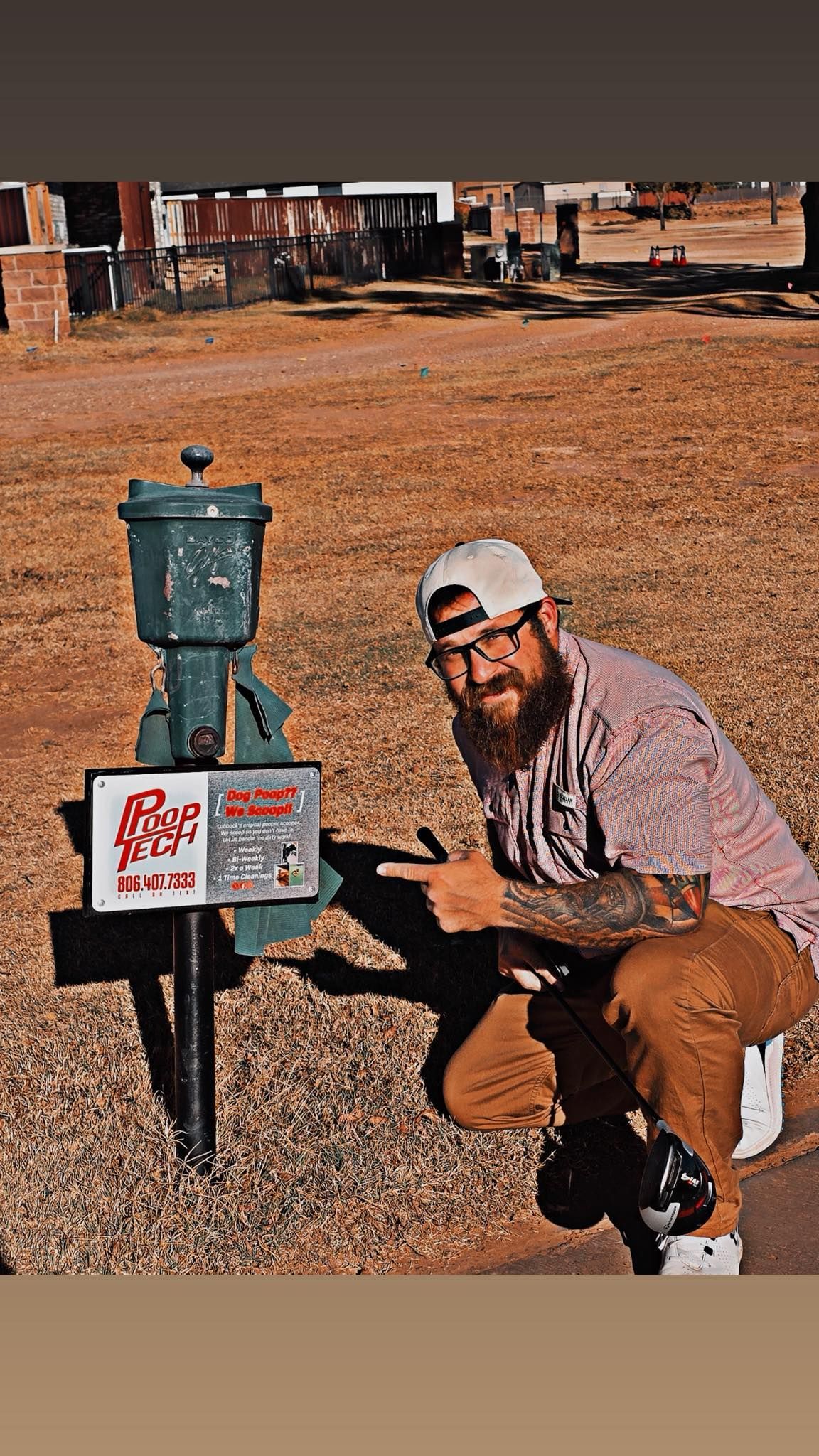 Man crouching beside a green utility box in a dry field with buildings in the background