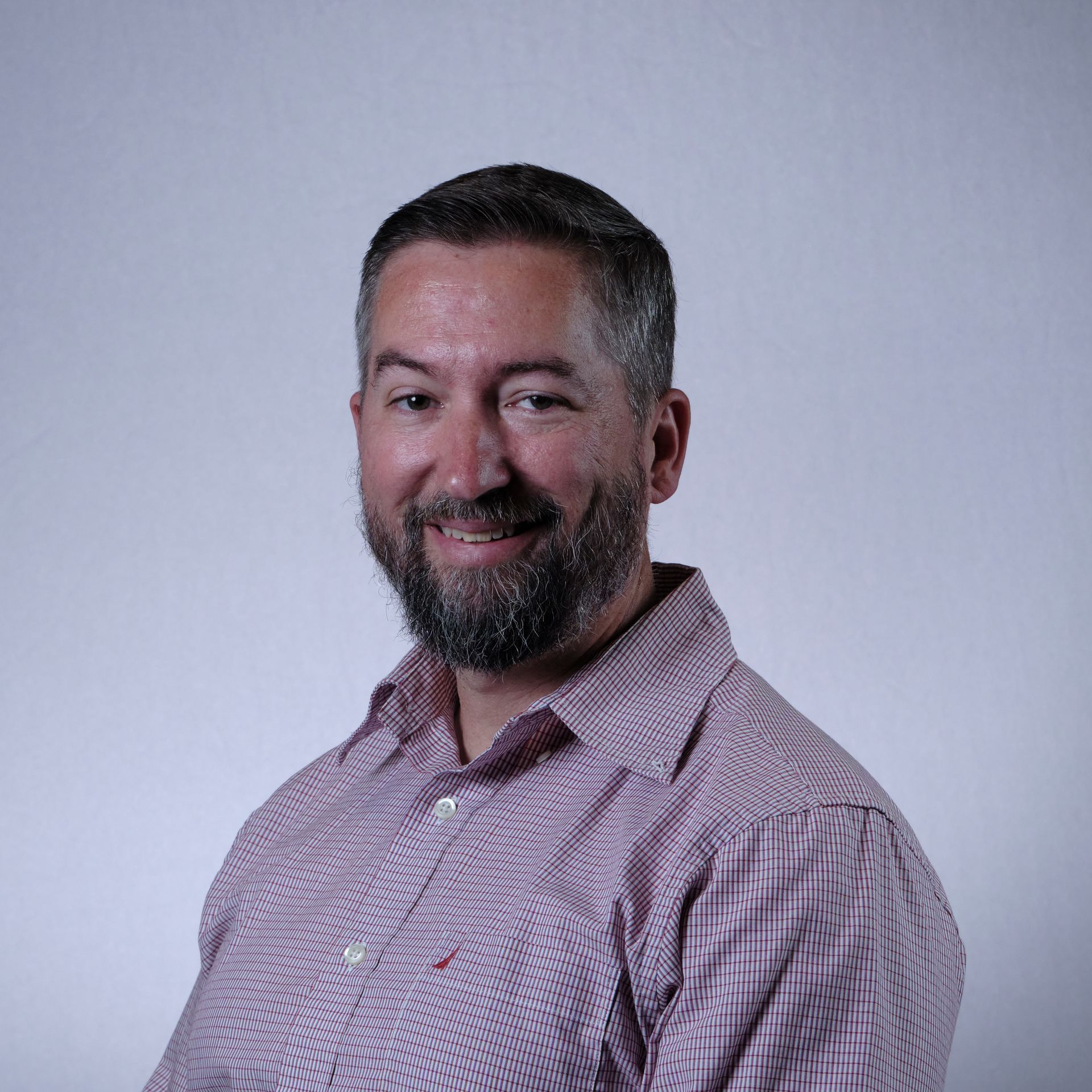 Smiling bearded man in a pink patterned shirt against a light gray background.