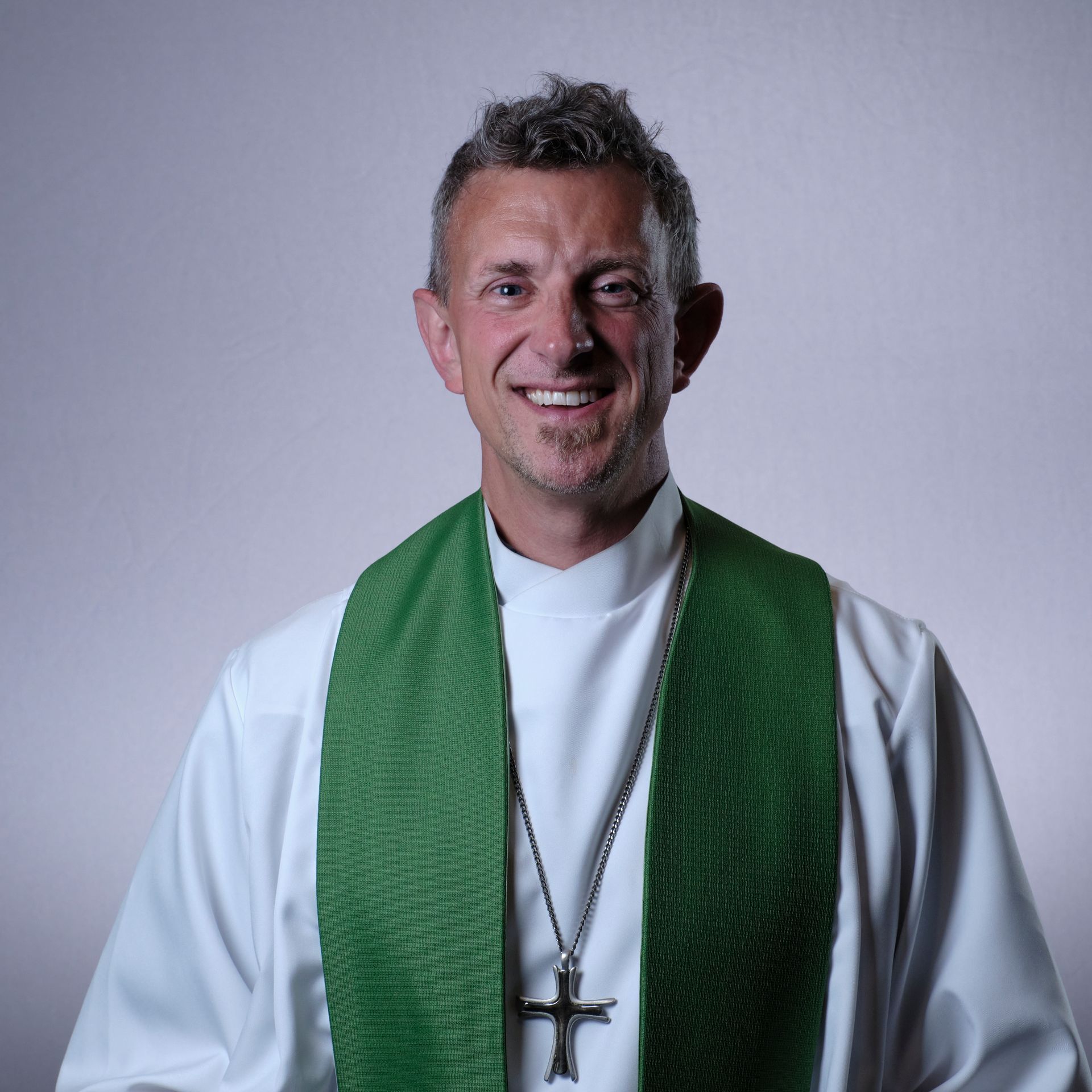 The pastor wearing a white shirt and a green vest with a cross necklace