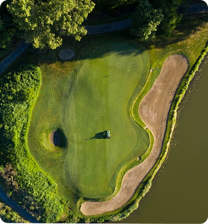 Overhead view of a golf green with sand traps, a lake, and a cart.