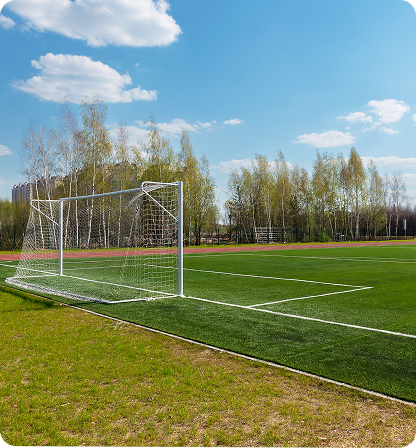 Soccer goal on green field under blue sky with trees.