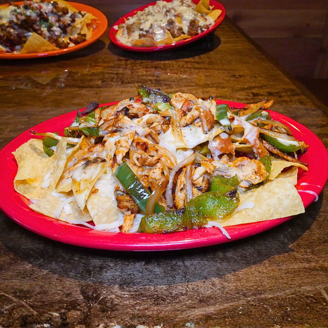 Nachos Fajitas: Grilled chicken or steak on crispy tortilla chips with sautéed vegetables, melted cheese, and toppings.
