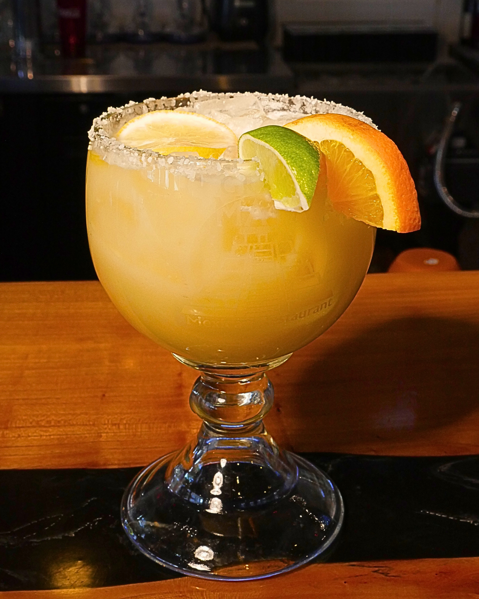 Lime margarita in a stemmed glass with a lime wedge and orange slice on a bar counter