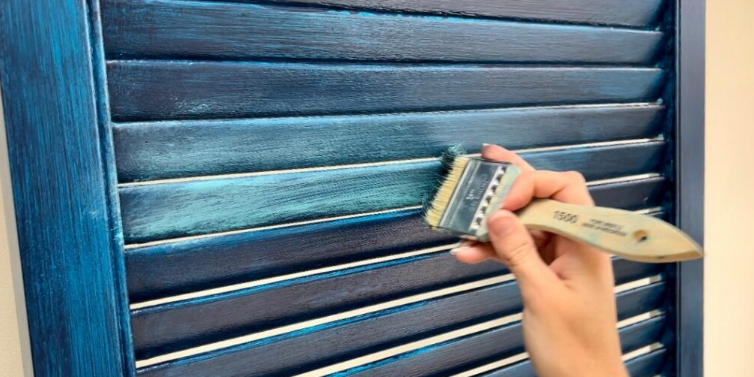 Hand painting a blue shutter with a wide brush