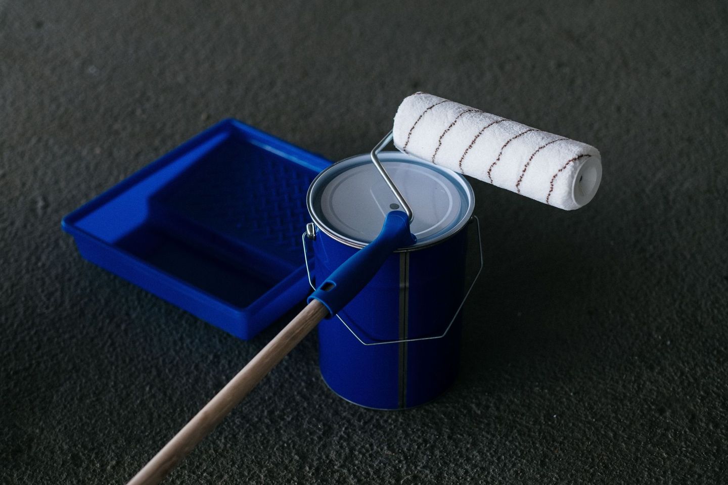 Paint roller and tray with blue paint on a dark surface