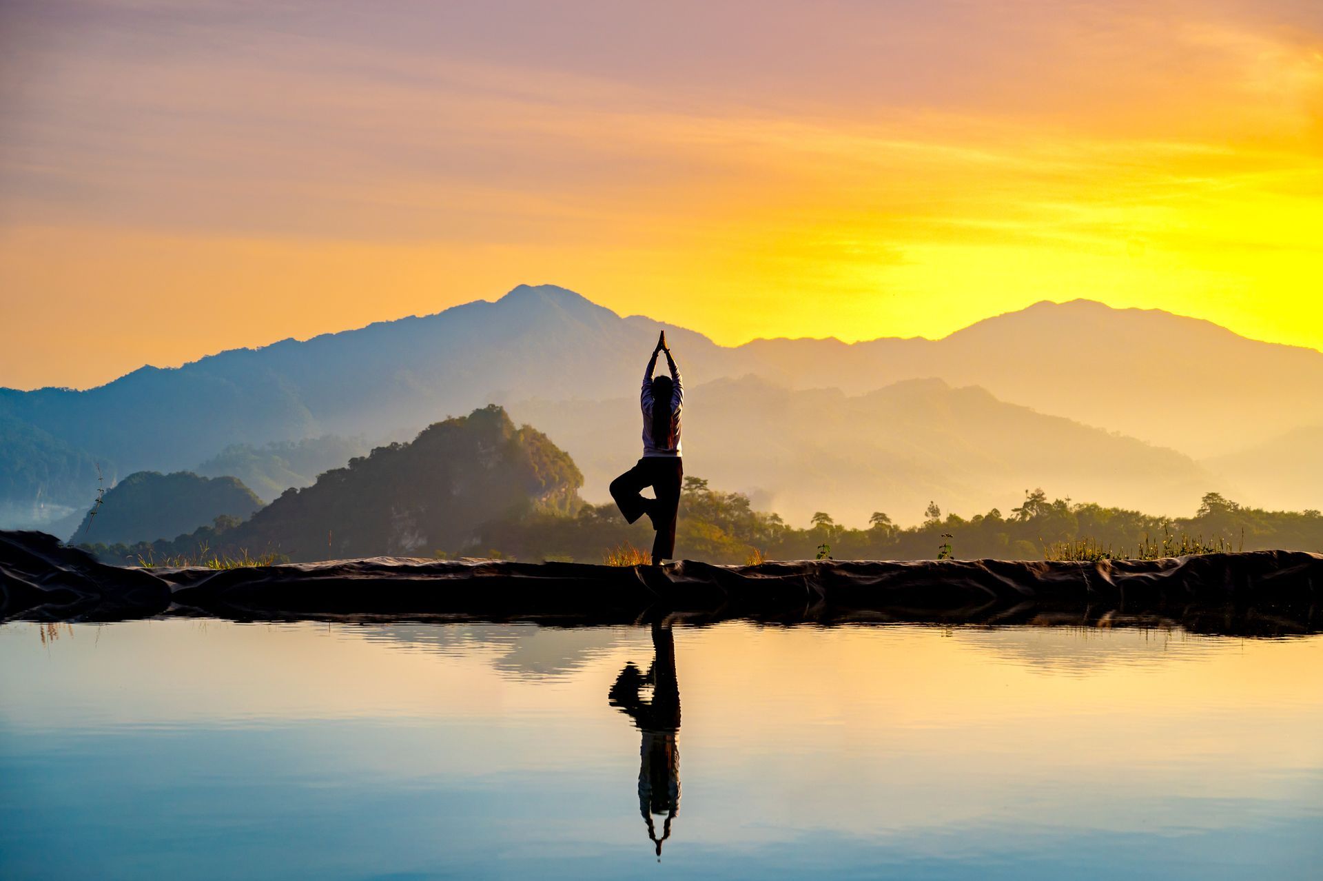 A person is practicing yoga in front of a lake at sunset.