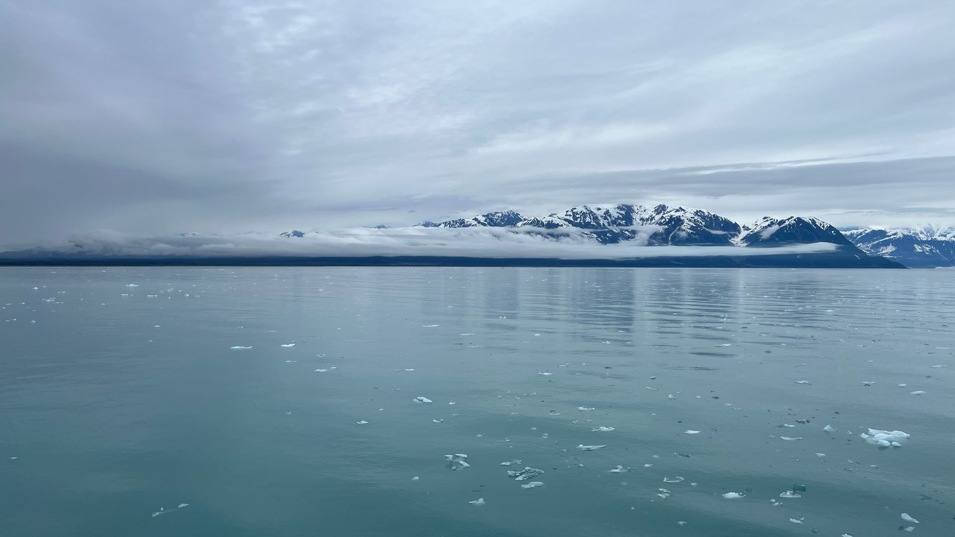 Calm icy blue sea under cloudy sky with distant snow-covered mountains