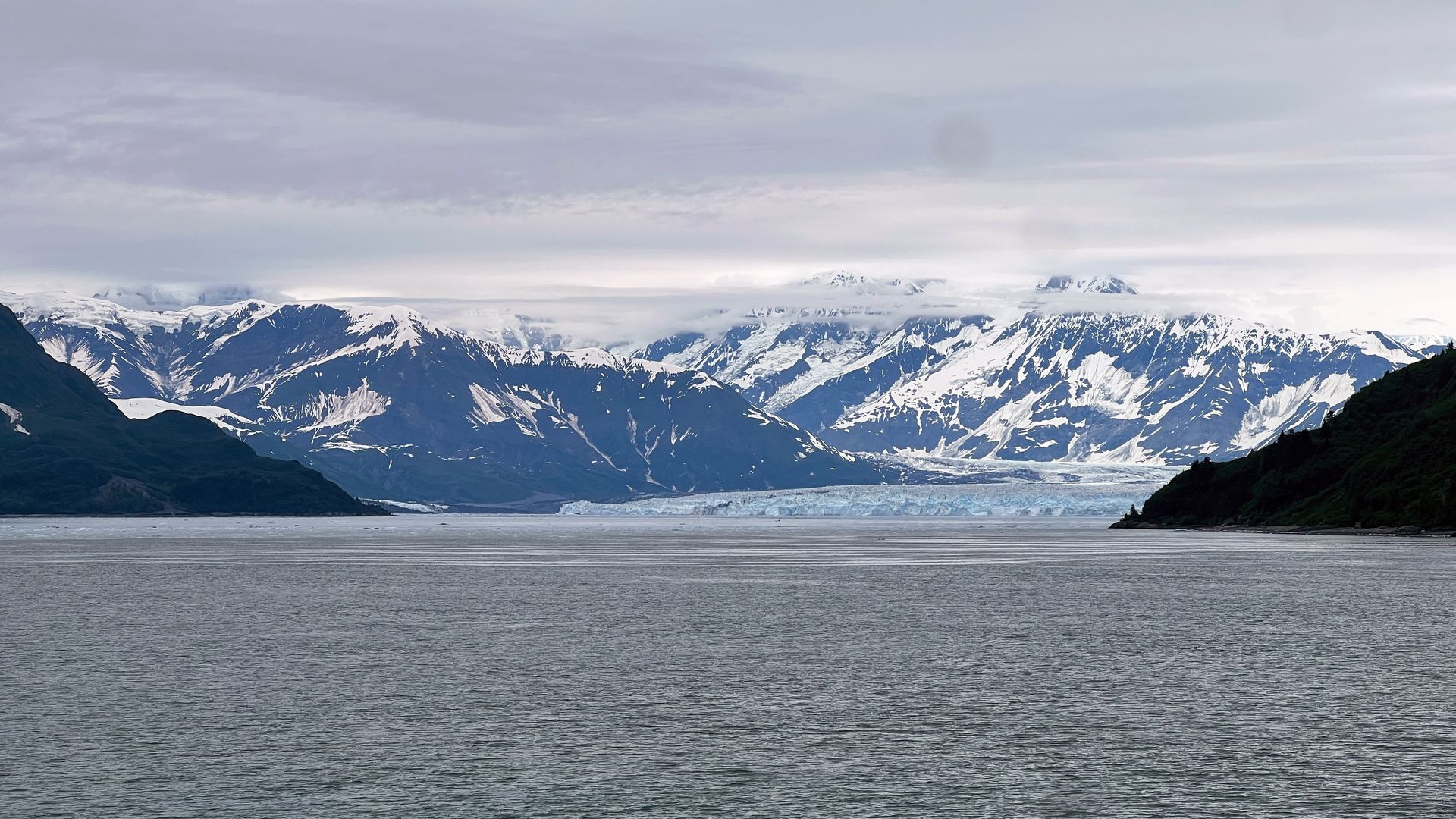 Snowy mountains across a calm fjord under an overcast sky