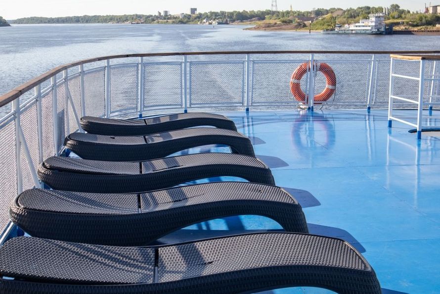 Ferry deck with black lounge chairs, white railing, and a lifebuoy beside calm water