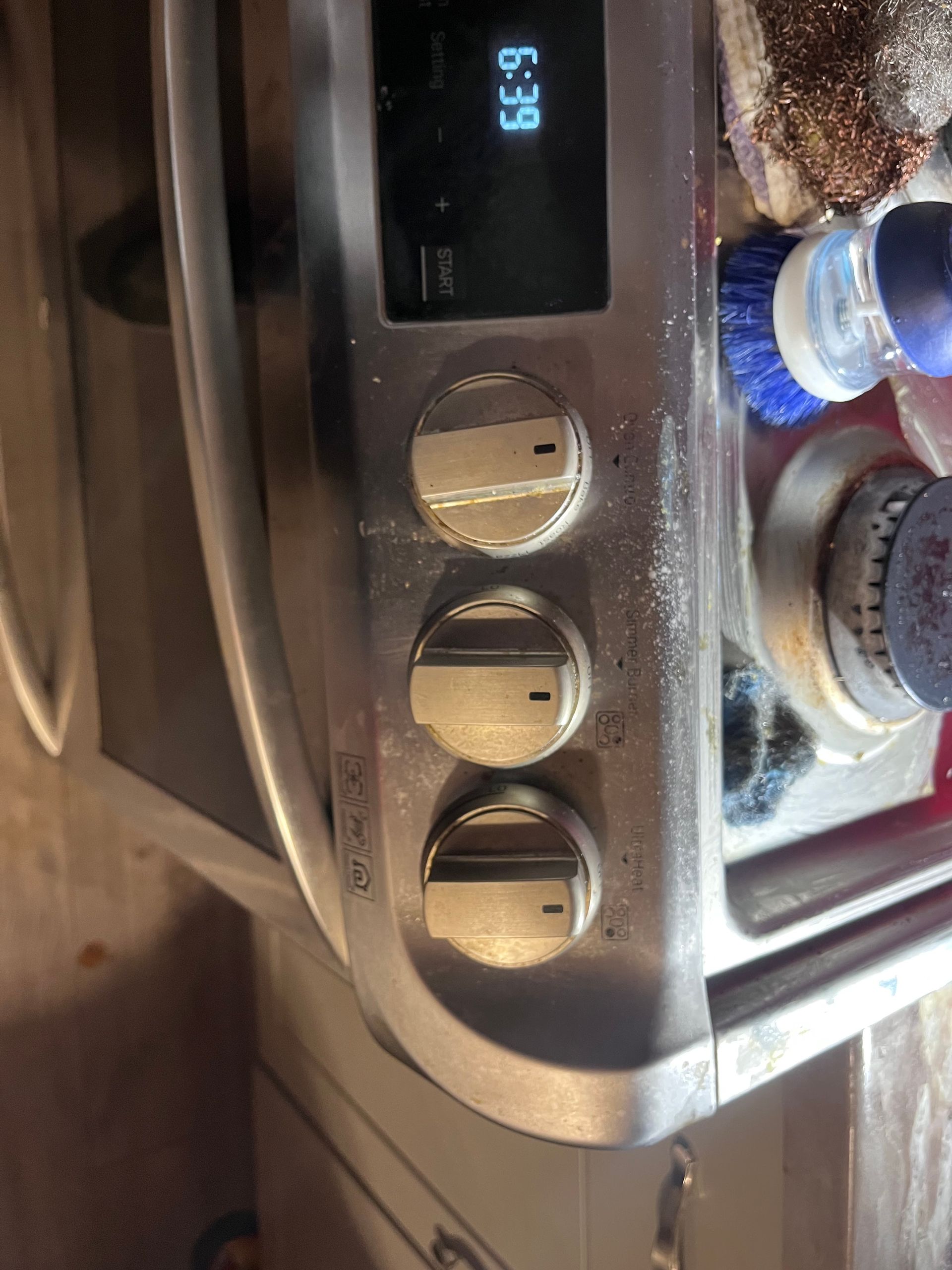 Close-up view of an oven control panel. The panel displays a digital clock at 6:39 and three silver knobs.