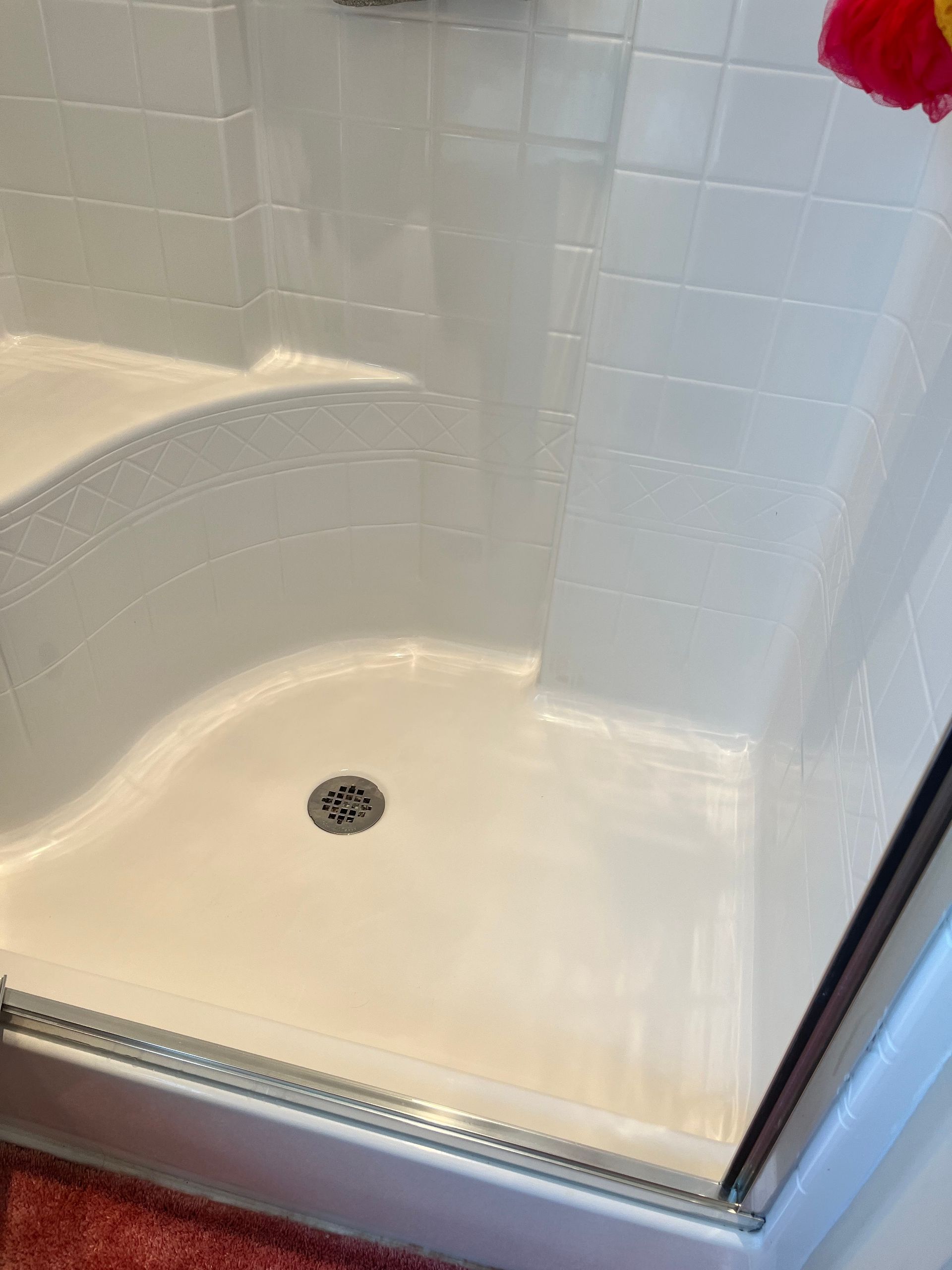 White-tiled shower with a curved bench seat, glass door, and drain.