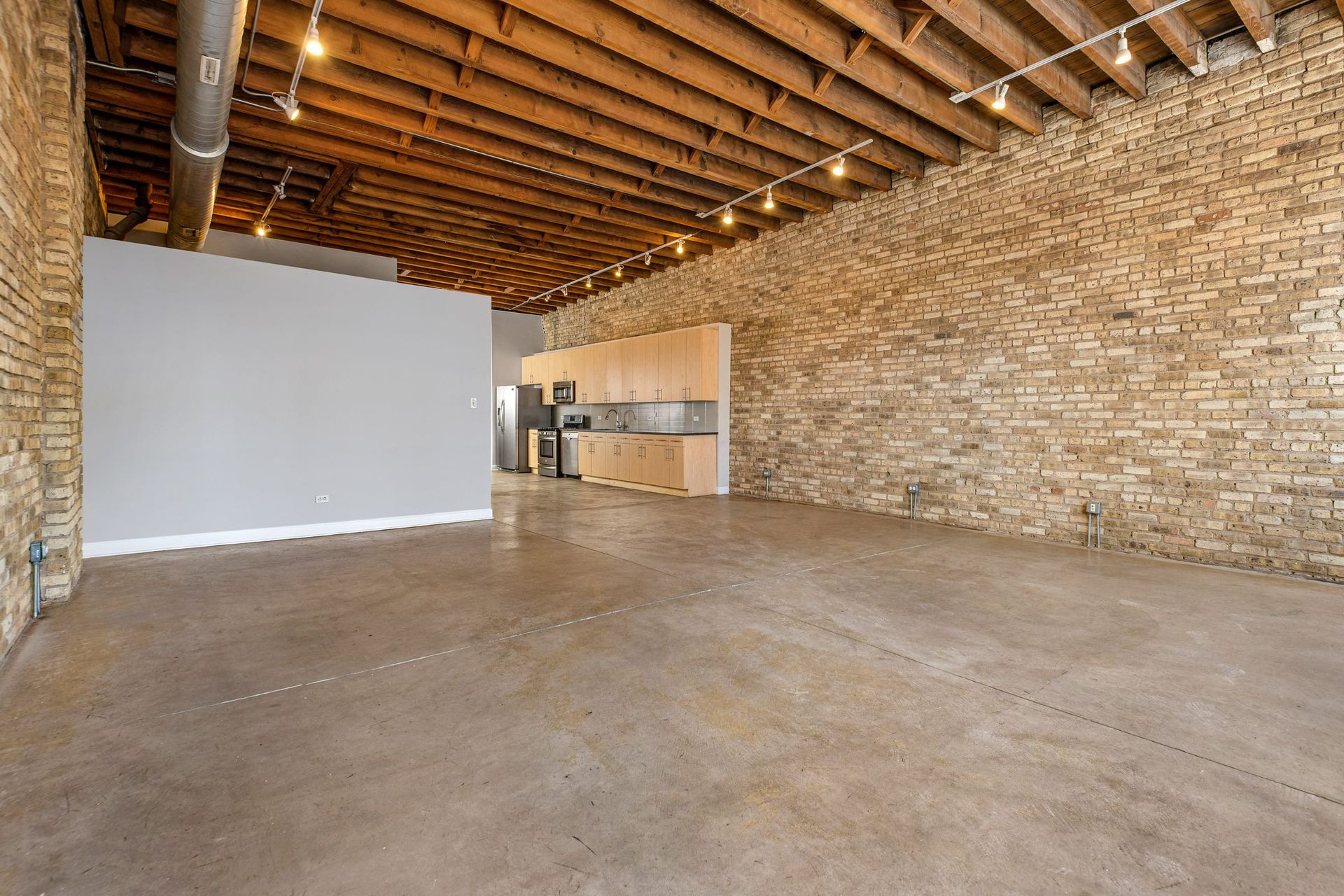 a large room with a brick wall and concrete floors and a kitchen