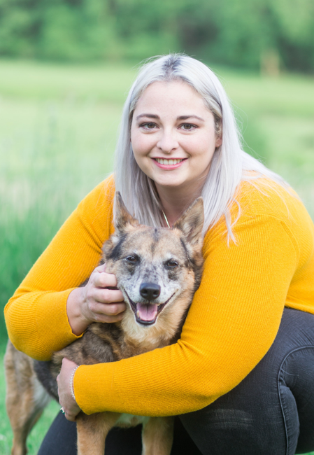 Dr. Jessi Turner in a yellow sweater is kneeling down and hugging a dog.
