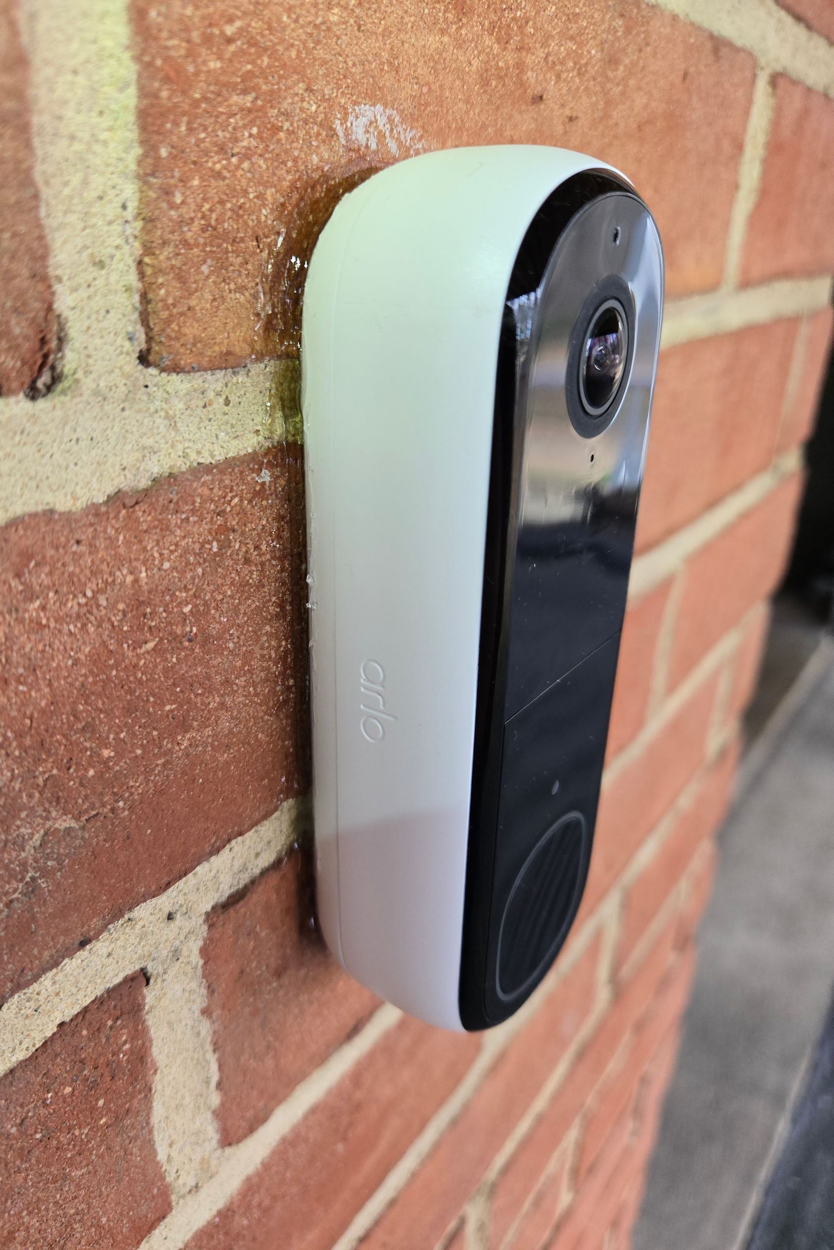 A white doorbell is attached to a brick wall.