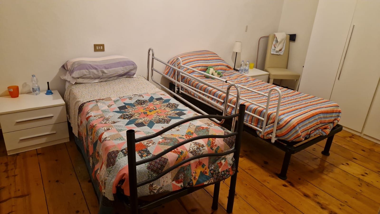 Due letti singoli in una stanza; uno con sponde, comodini e trapunte floreali. Pavimenti in legno.