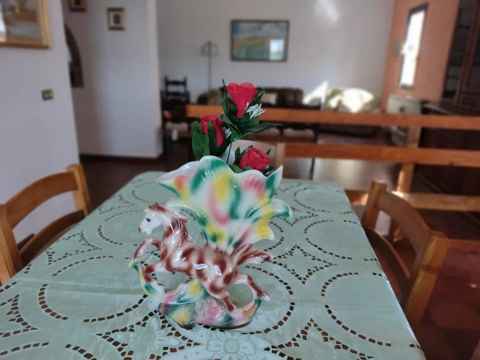 Un vaso di fiori con fiori rossi su un tavolo. La stanza è arredata con mobili in legno e ha una finestra.