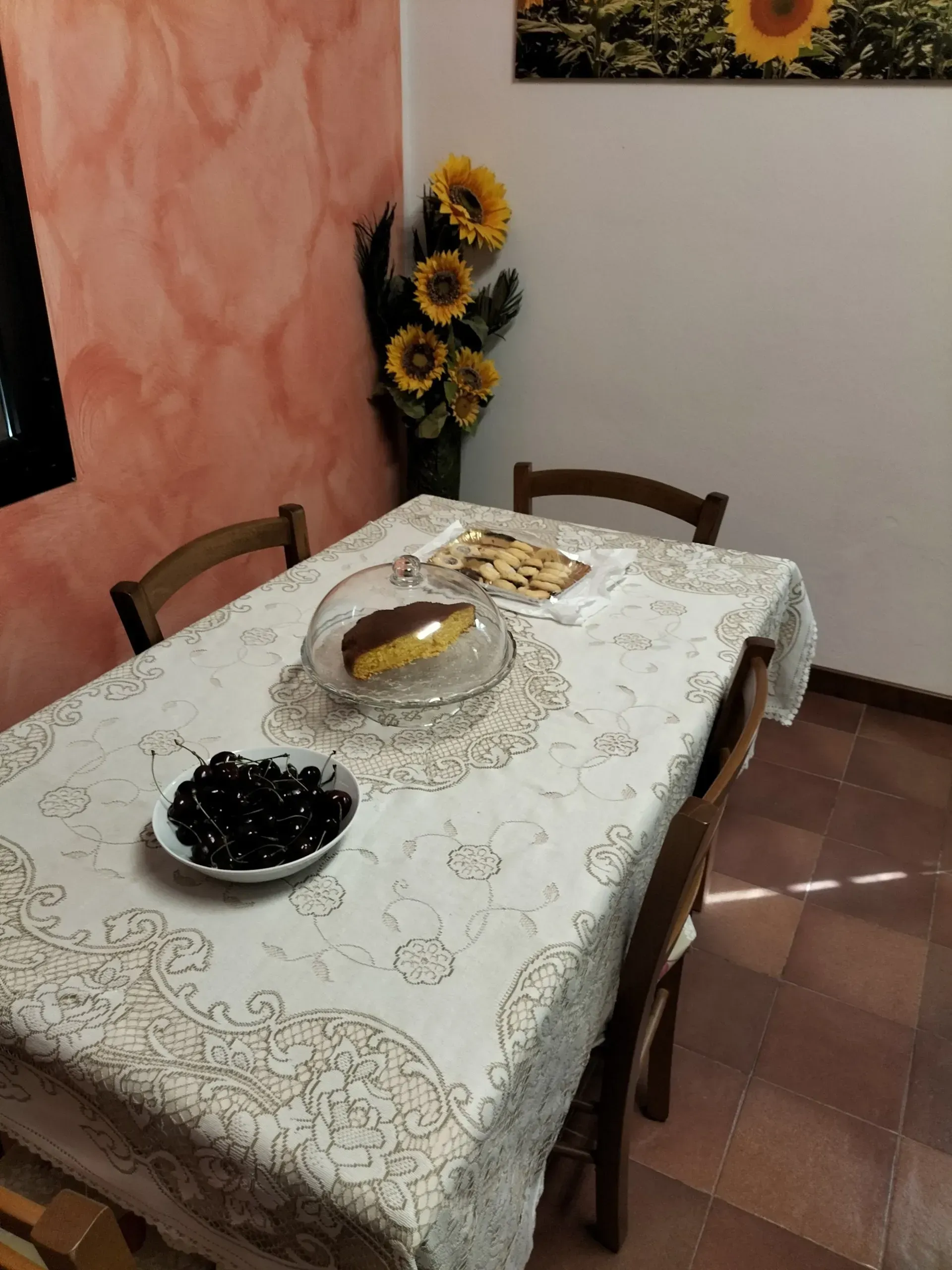 Tavolo da pranzo apparecchiato con torta, ciliegie e girasoli; parete color pesca.