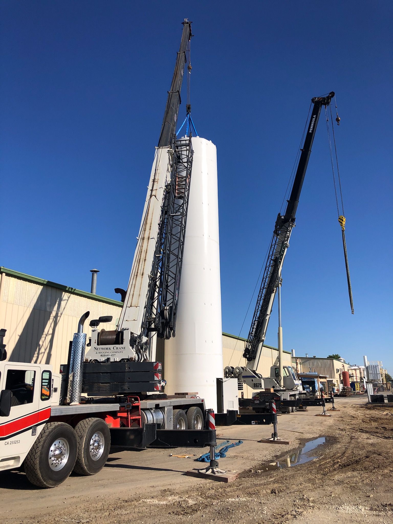 A crane is lifting a large white cylinder in a parking lot.