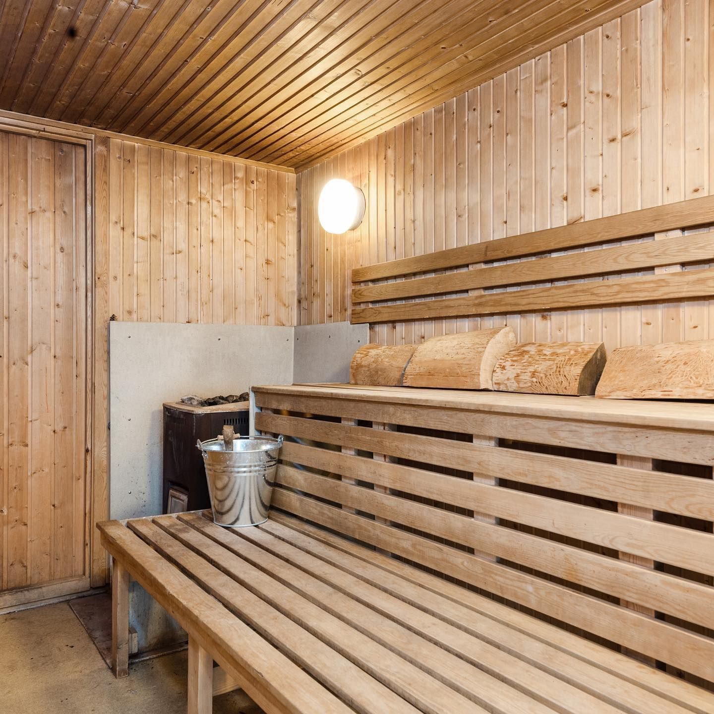 A wooden bench in a wooden sauna with a bucket on the bench.