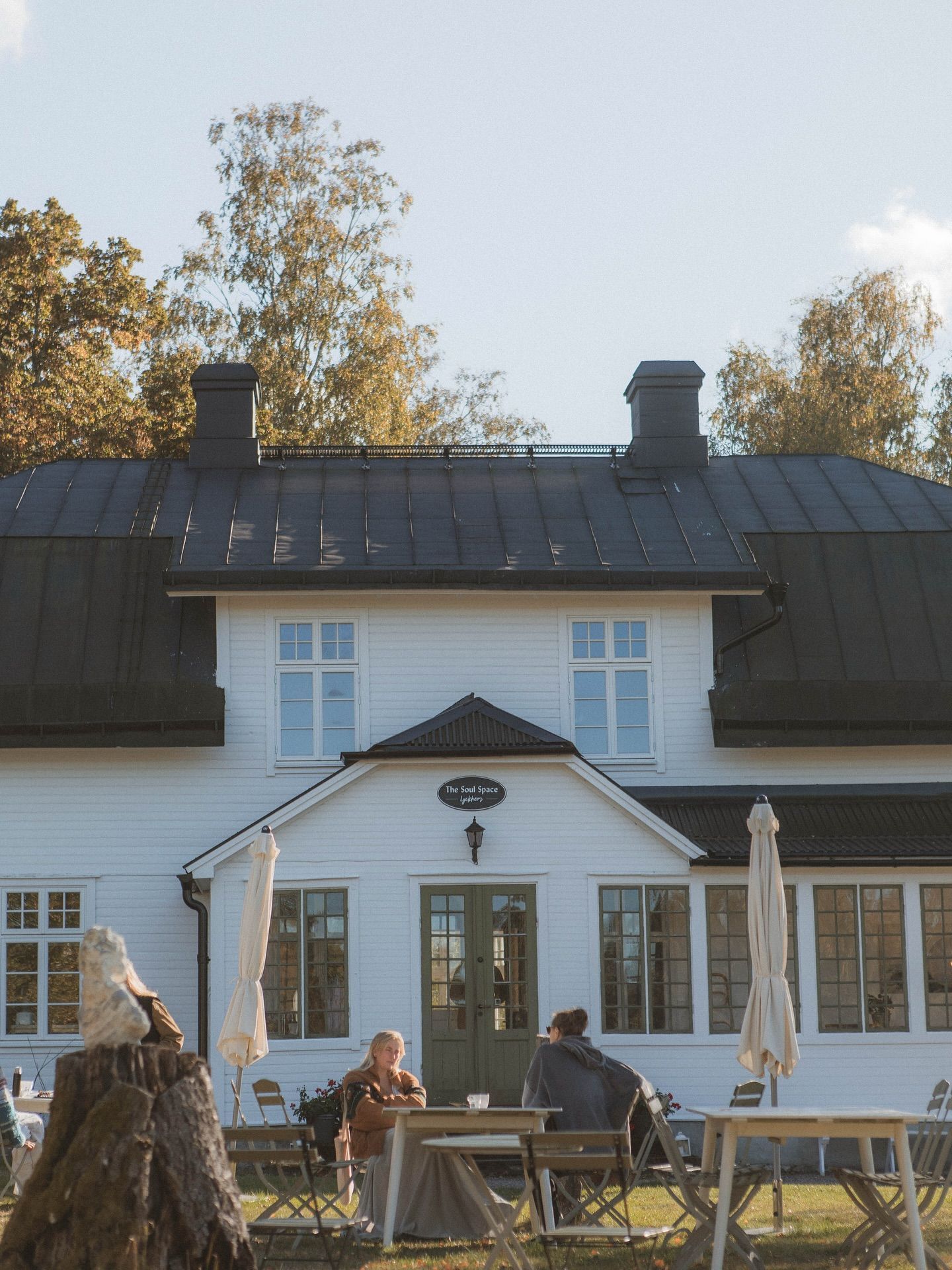 A white house with a black roof is surrounded by tables and chairs