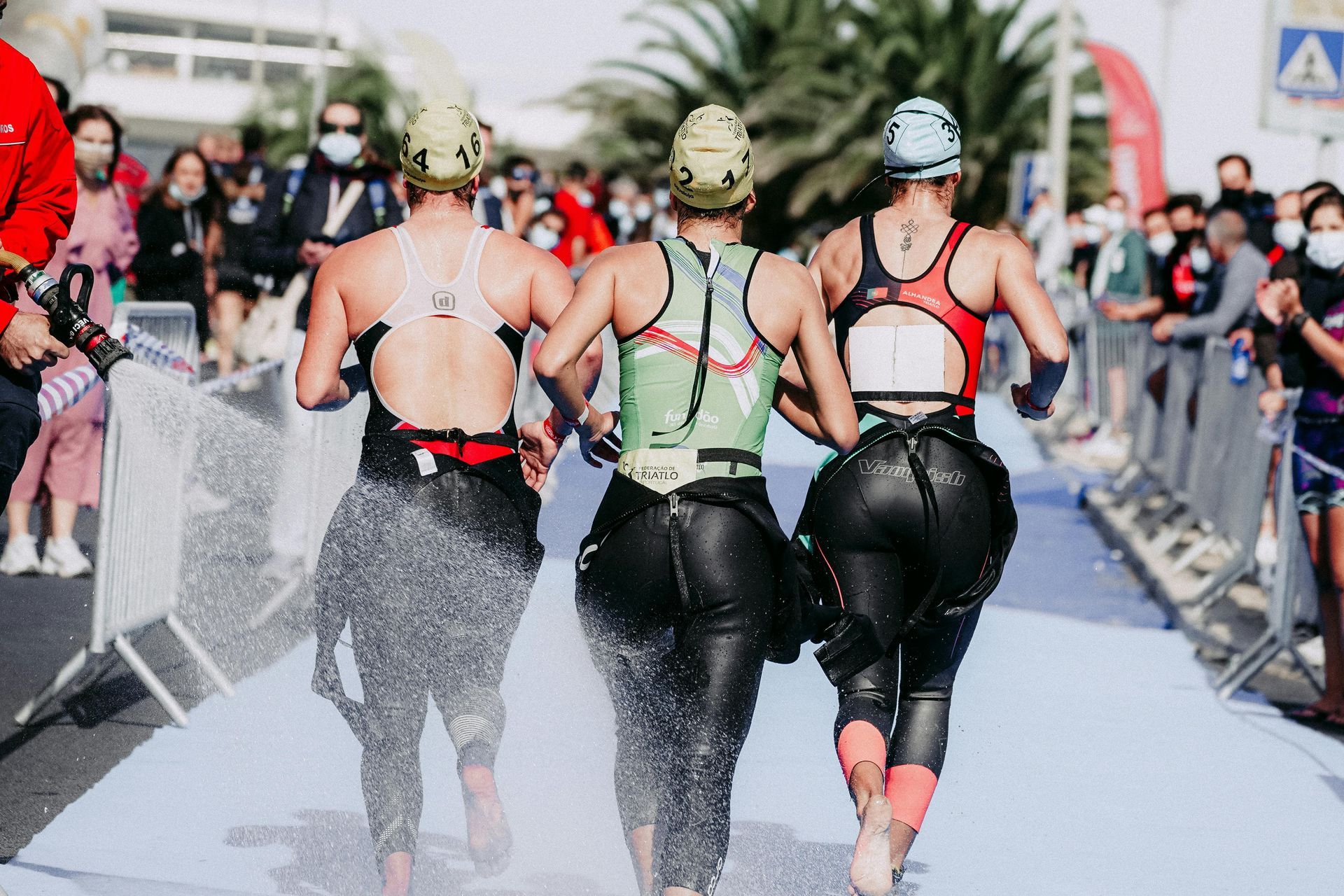 Three roller skaters race down a wet street, spraying water in a crowded outdoor event.