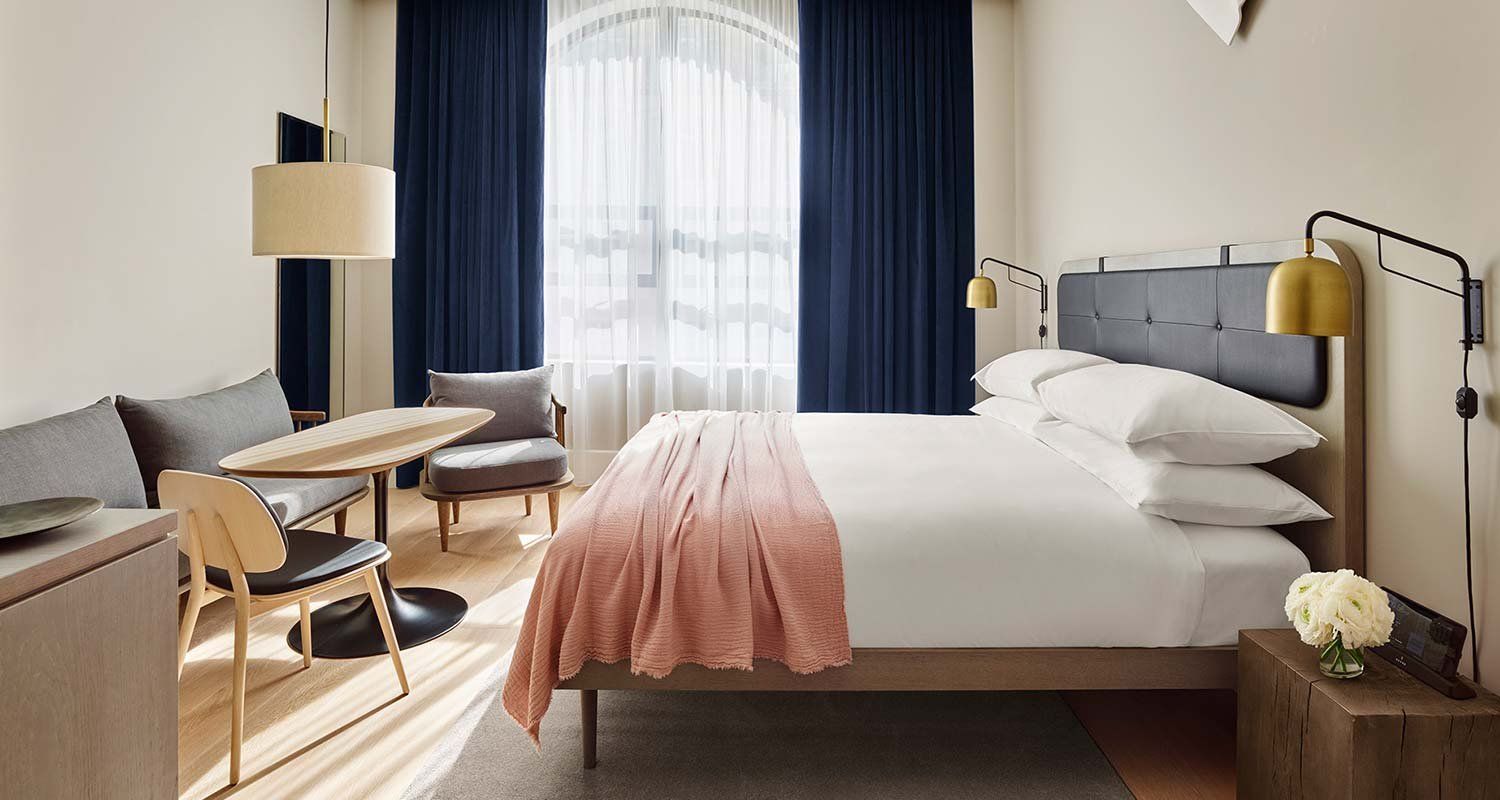 A hotel room with a bed, sofa, table, and chair.