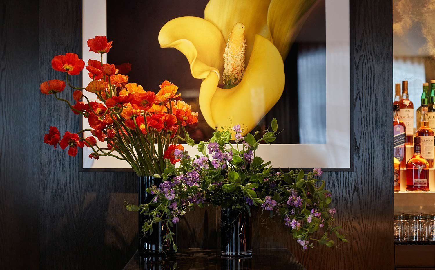 Yellow floral sculpture behind vases of red, orange, and purple flowers on a display shelf