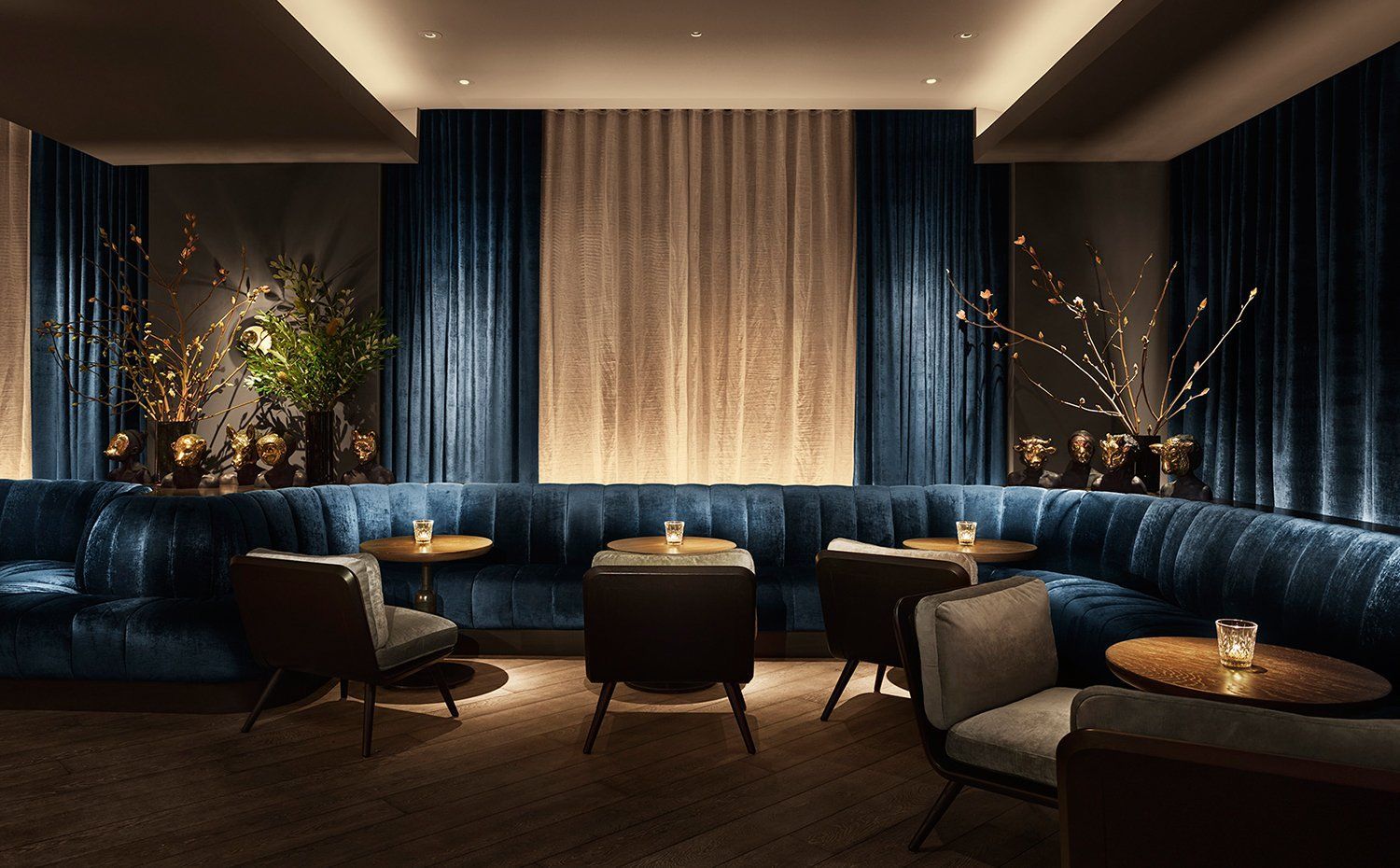 A luxurious lounge with a blue velvet sofa, wooden tables, and candles.