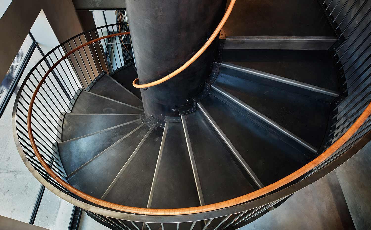 Spiral metal staircase with black steps and a curved wooden handrail viewed from above