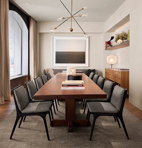 Modern dining room with a long wooden table, gray chairs, and a pendant light above.