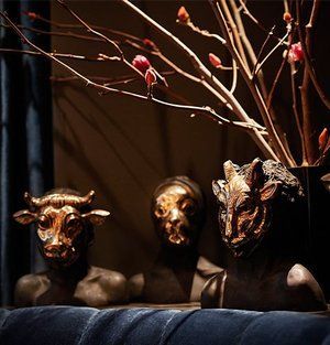 Three dark animal busts beneath bare branches, lit warmly against a black background